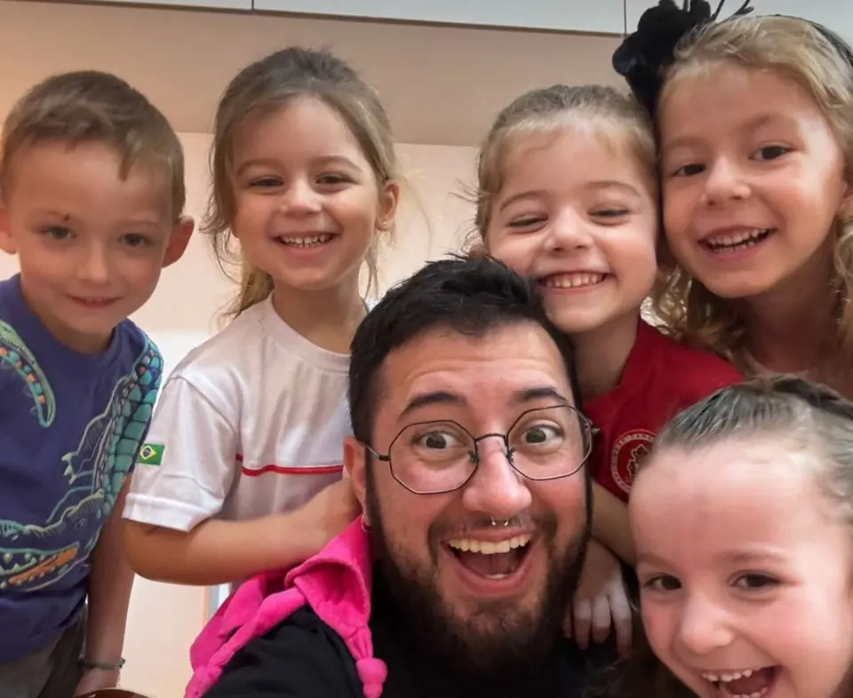 Lucca Iarcheski cercado por cinco crianças sorrindo, numa aula de musicalização